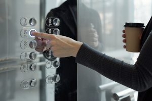 Hand of young businesswoman with drink pushing button of elevator
